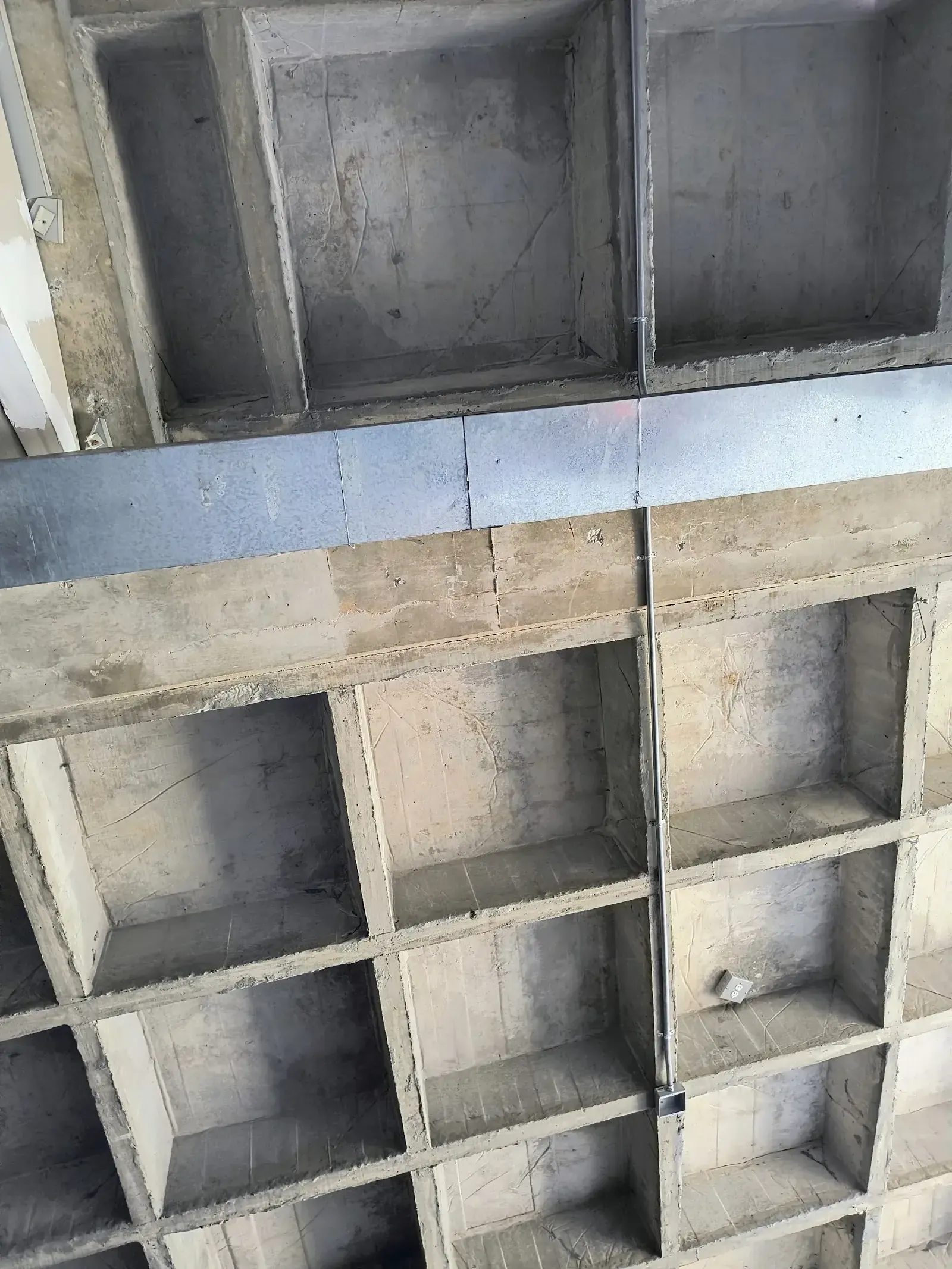 Tubería metálica de canalización y ducto galvanizado tendidos bajo una placa de concreto reticular en la nave industrial
