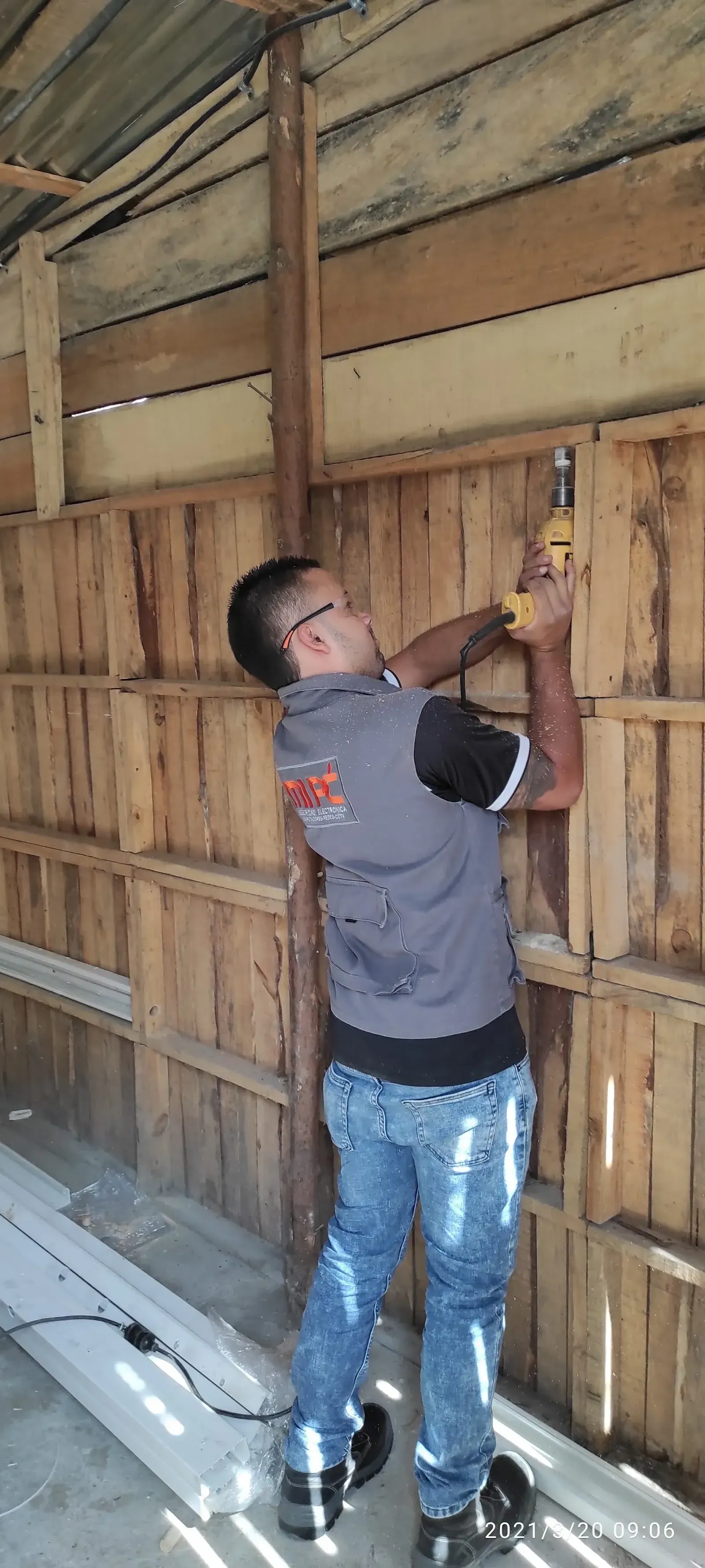 Técnico de MiPC Tecnología con chaleco de la empresa perfora la pared de madera de la construcción para pasar el cableado
