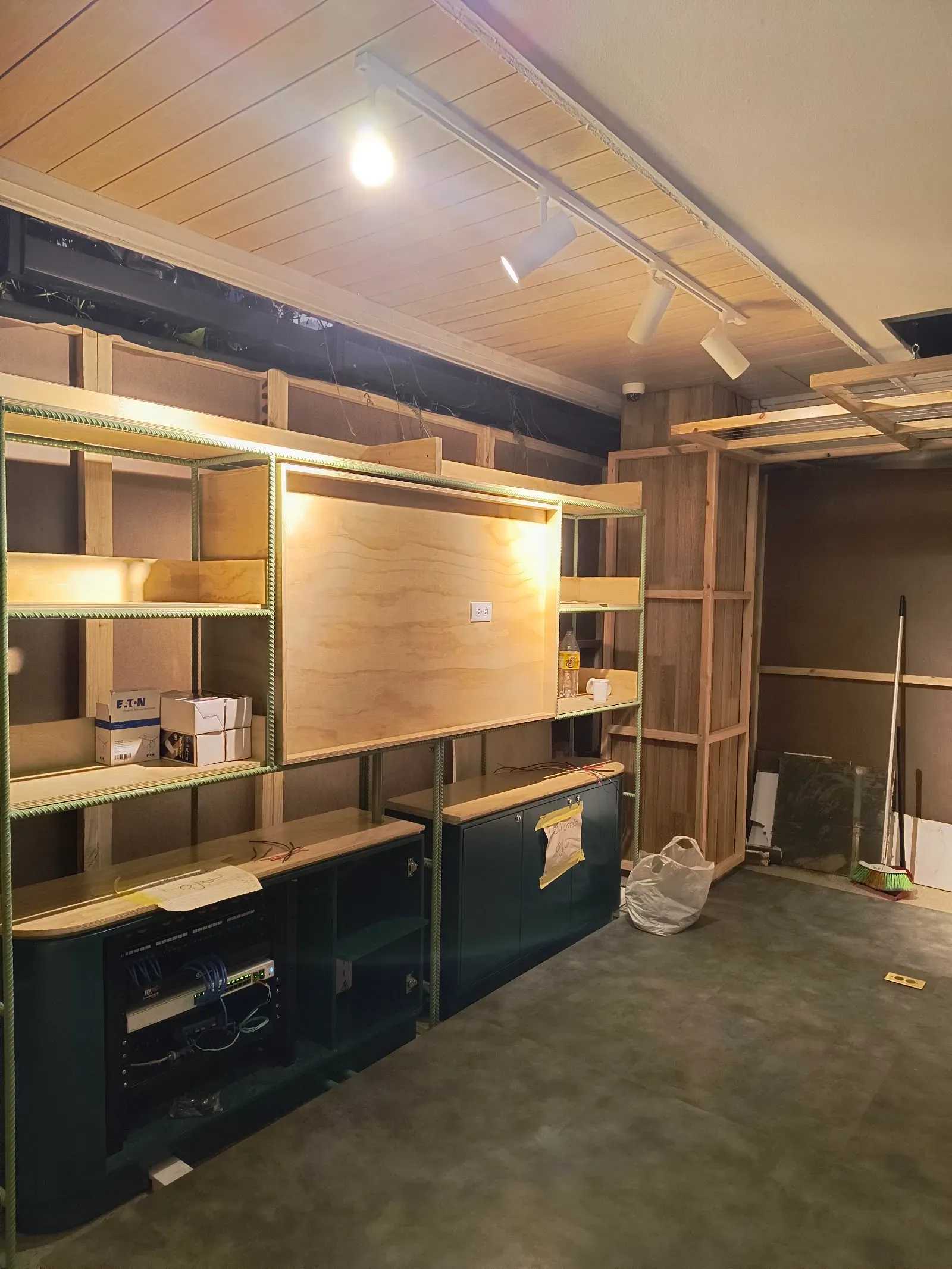 Punto de información terminado en el centro comercial: mueble de madera con estantería iluminada, riel de luces encendido en el cielo raso y, en el mueble inferior abierto, el rack con su patch panel y su switch integrados